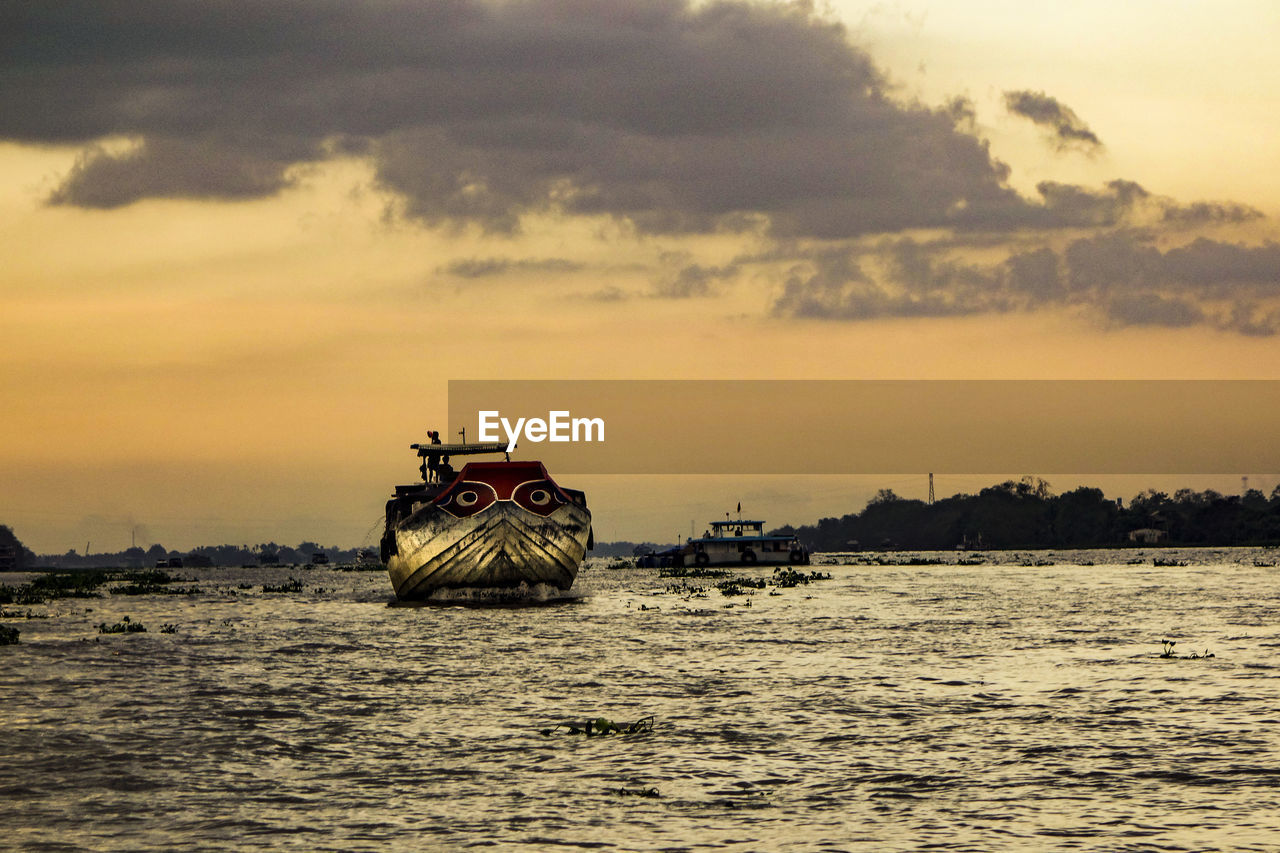 Silhouette boat in river against sky during sunset