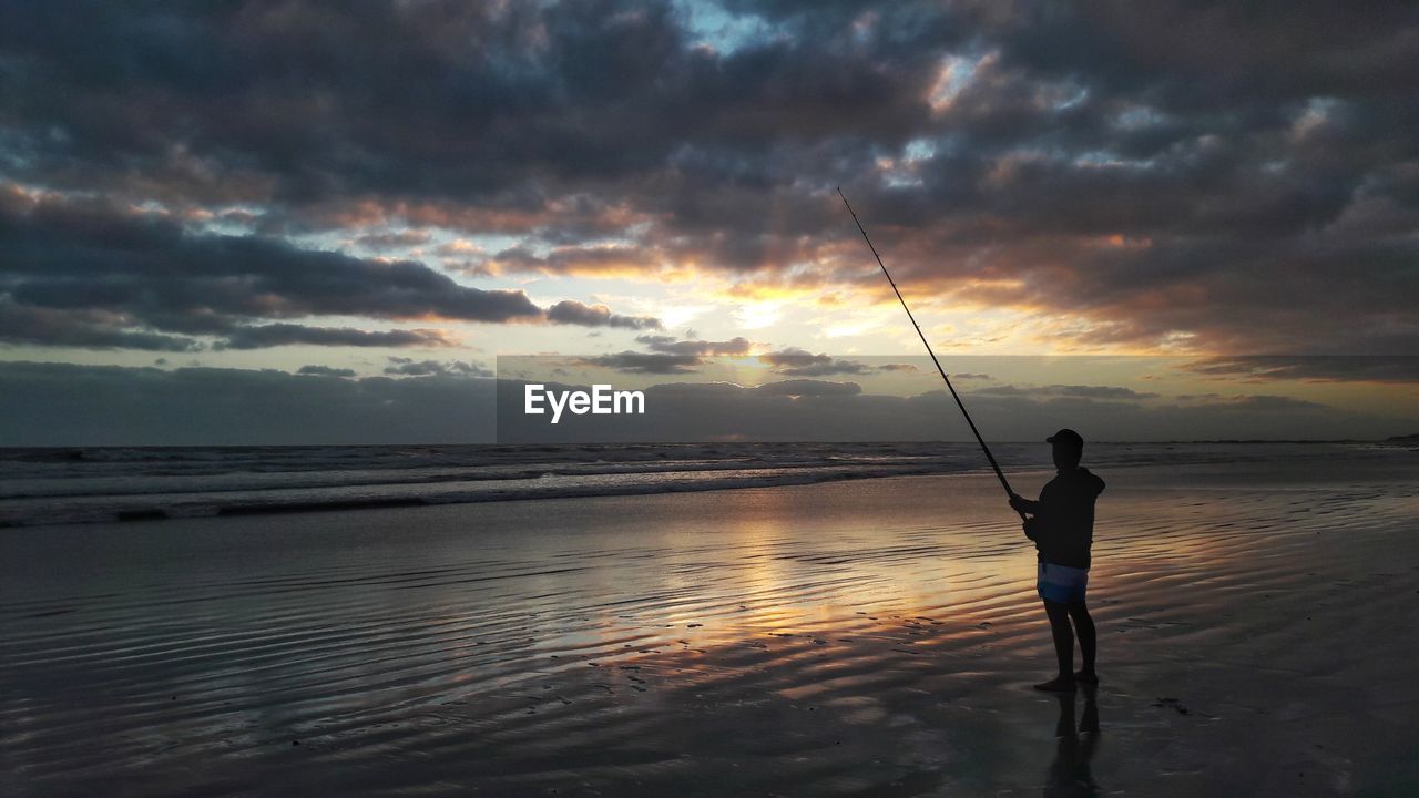 MAN FISHING ON BEACH AT SUNSET