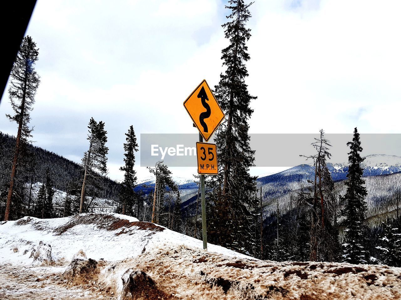 Road sign against snow covered mountain against sky