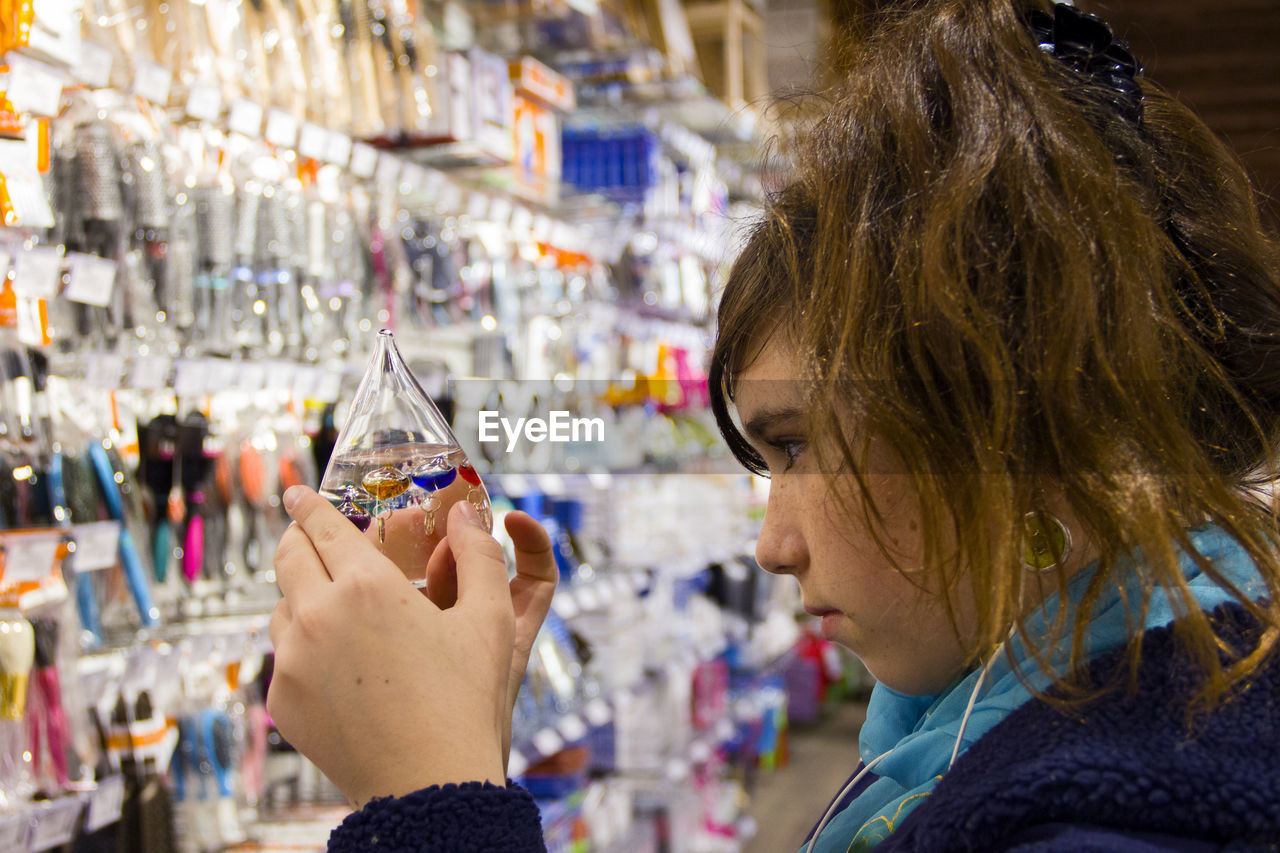 Side view of young woman looking at galileo thermometer at store
