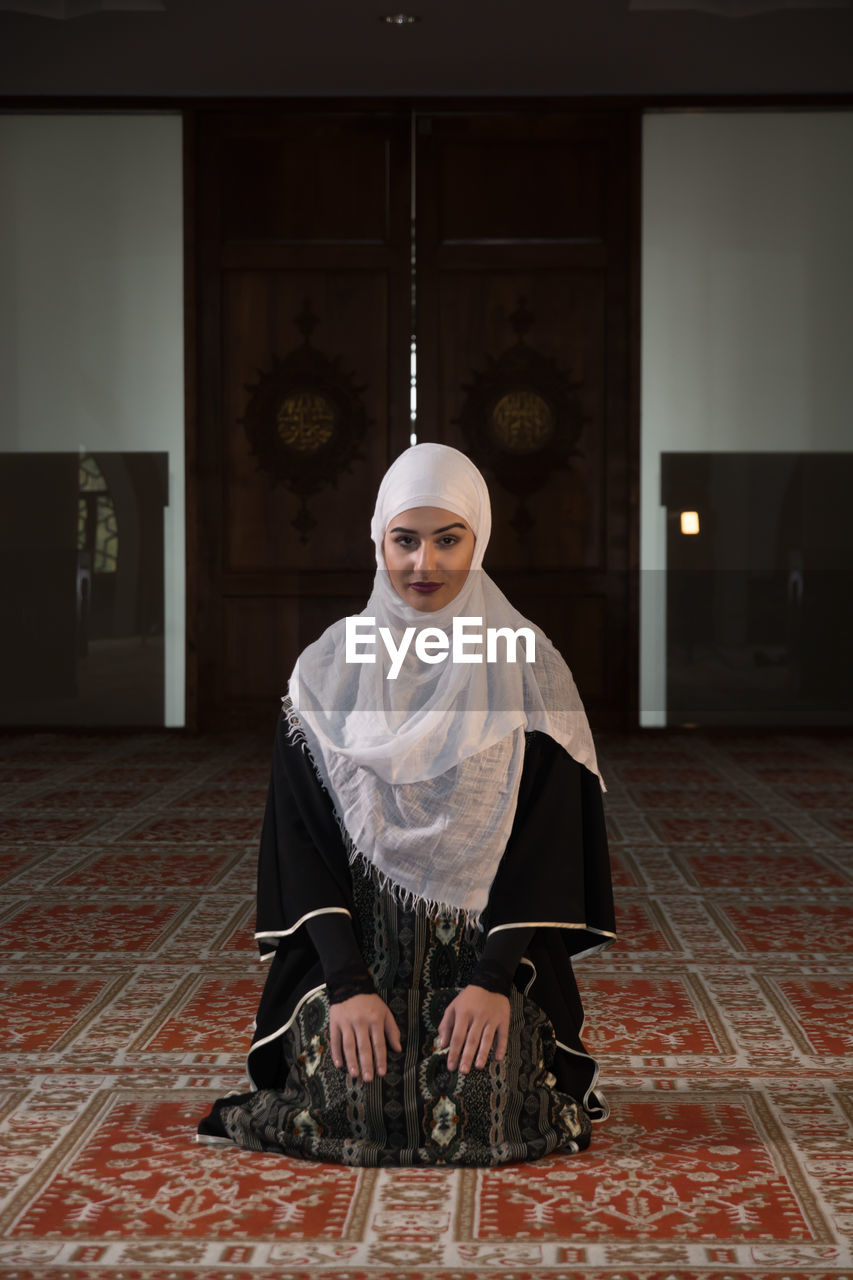 Woman in burka praying while kneeling on carpet