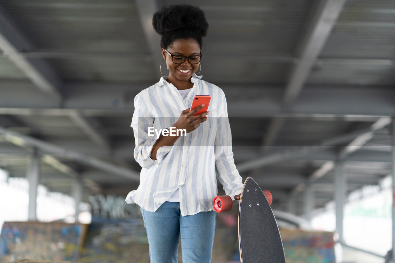 Smiling woman using mobile phone with skateboard