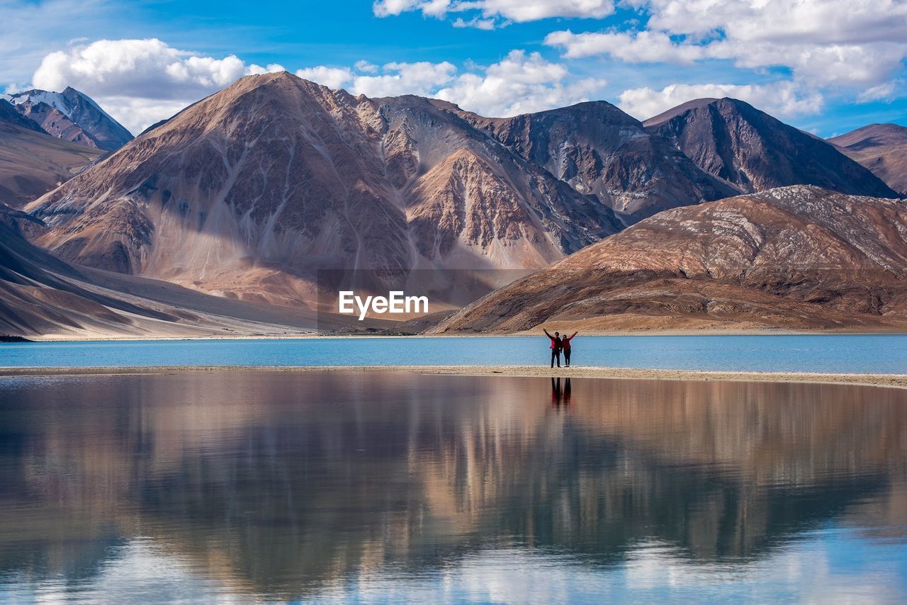 Man and woman standing at lake against mountains 