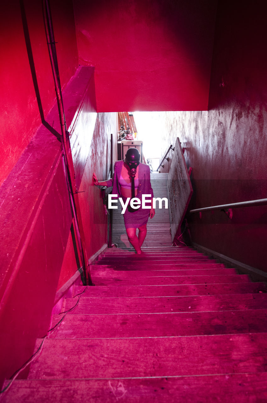 High angle view of woman with gas mask walking on illuminated steps in building