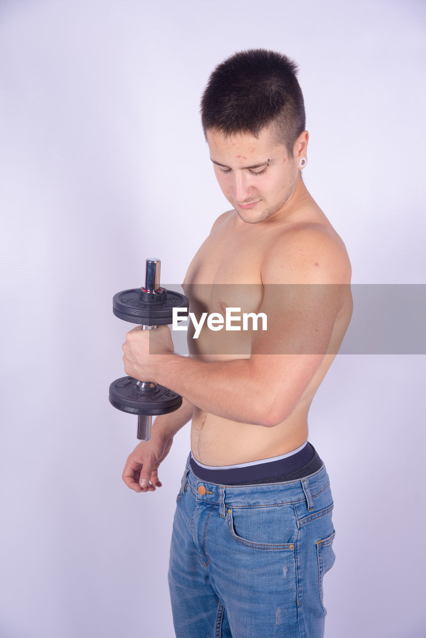 Shirtless man lifting dumbbells against purple background