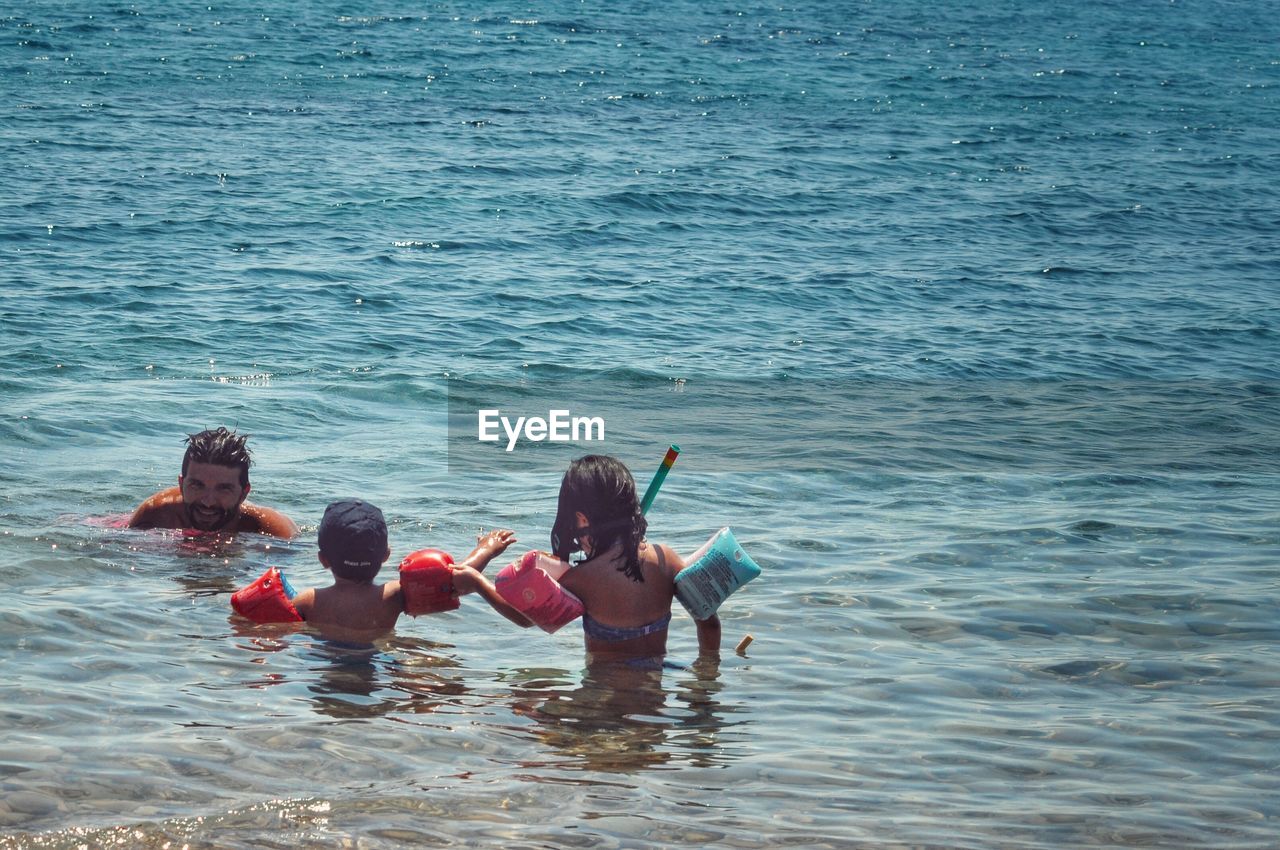 Shirtless father with children in sea