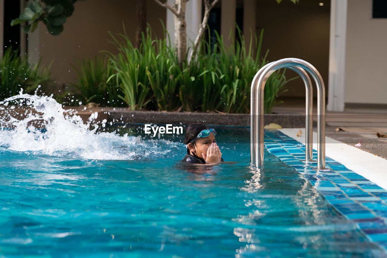 Girl with hands covering nose swimming in pool