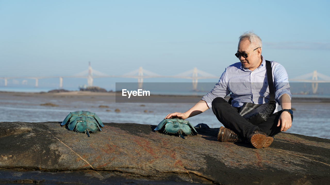 Portrait of man sitting on rock at beach