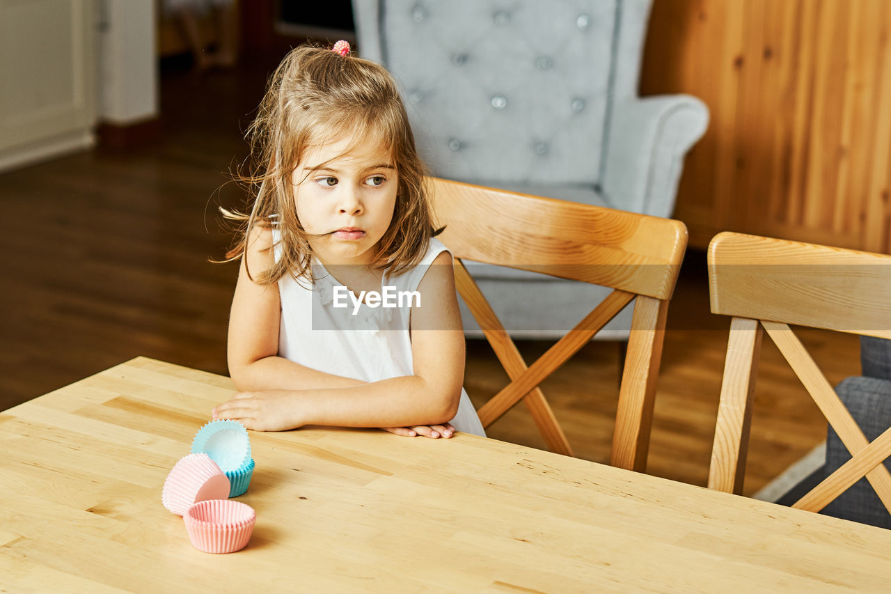 Cute girl looking away while sitting on table