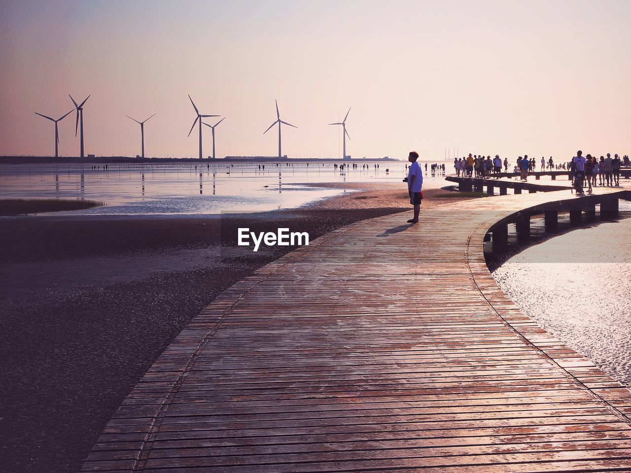 PEOPLE WALKING ON SEA SHORE AGAINST SKY