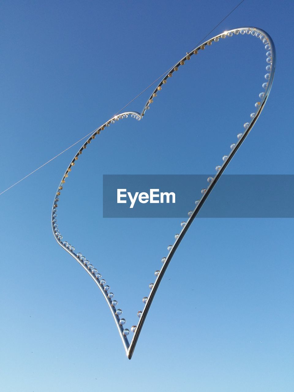 Low angle view of heart shape string light hanging against clear sky on sunny day