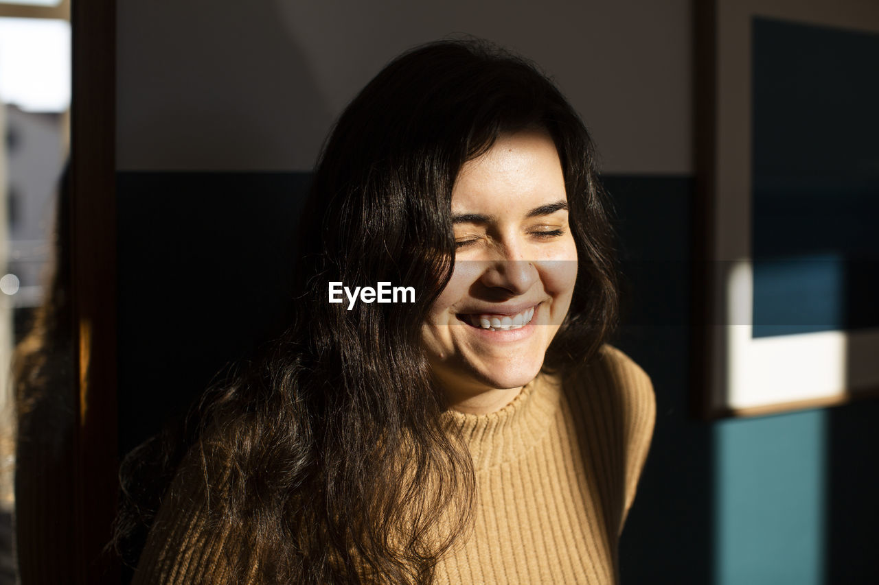 Happy young woman with eyes closed enjoying sunlight at home