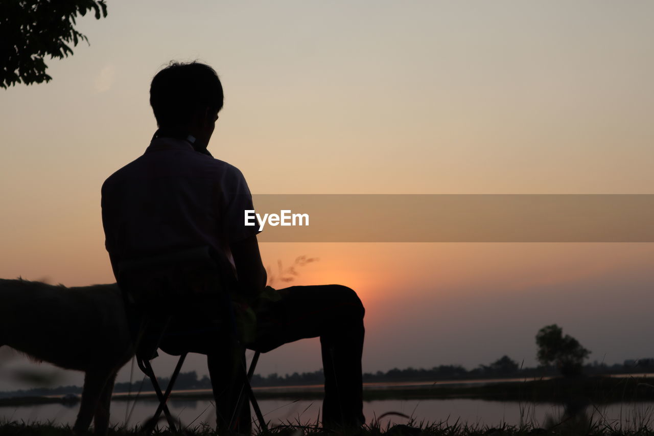 Side view of silhouette man sitting on field against sky during sunset