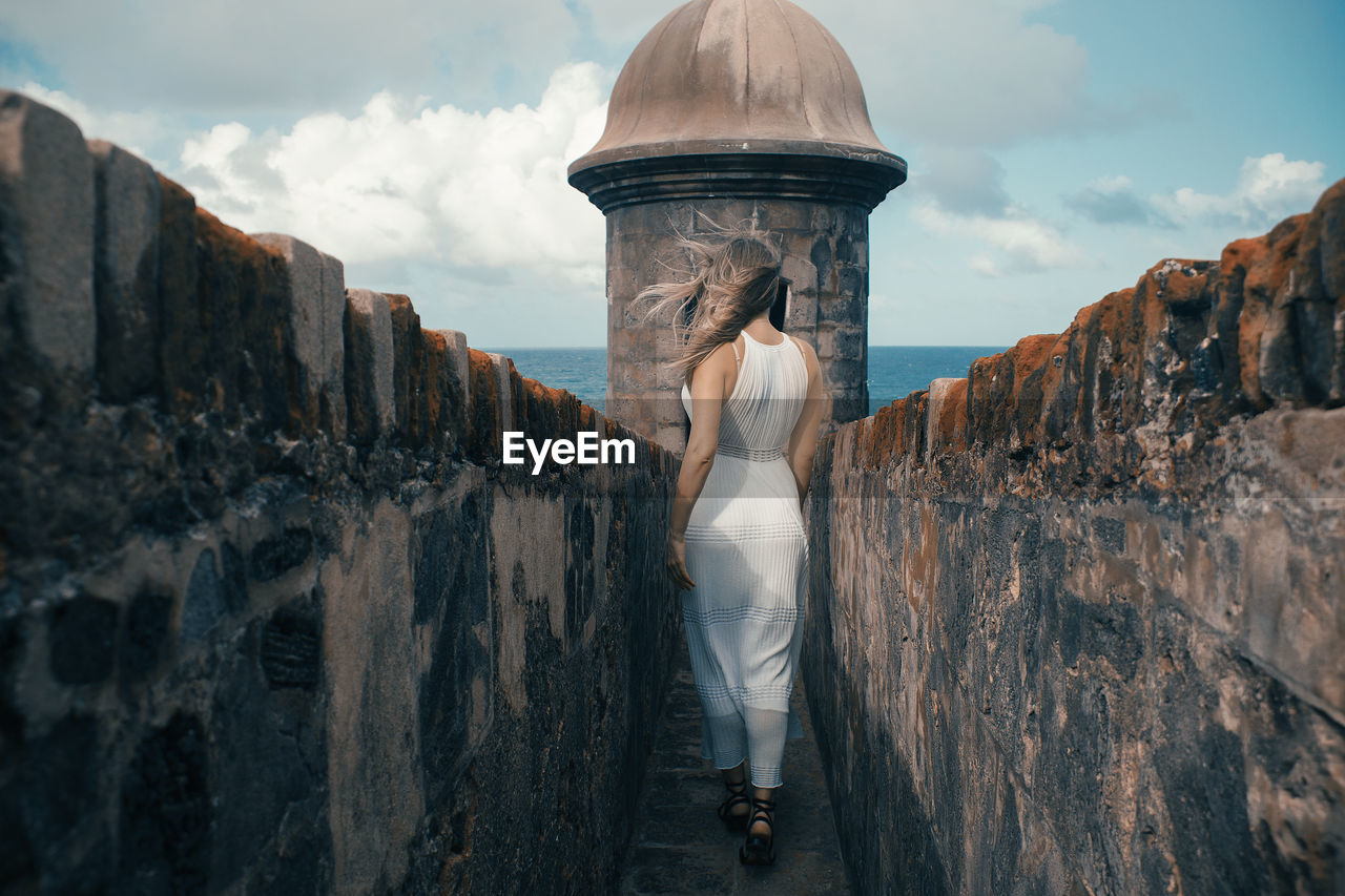 Rear view of woman walking amidst wall against sky