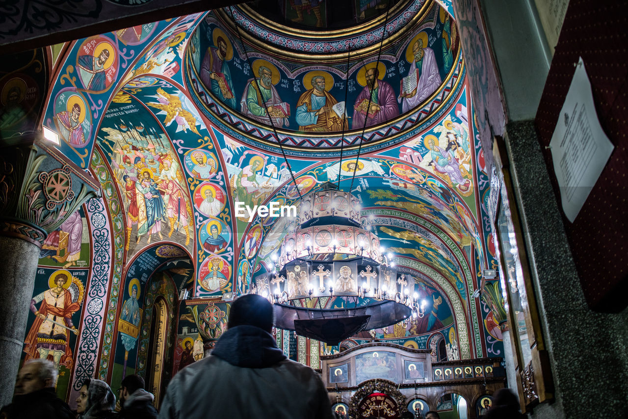 architecture, religion, built structure, belief, place of worship, spirituality, building, indoors, multi colored, rear view, travel destinations, stained glass, clothing, catholicism, person, creativity, adult, worship, art, low angle view, one person, praying, pattern