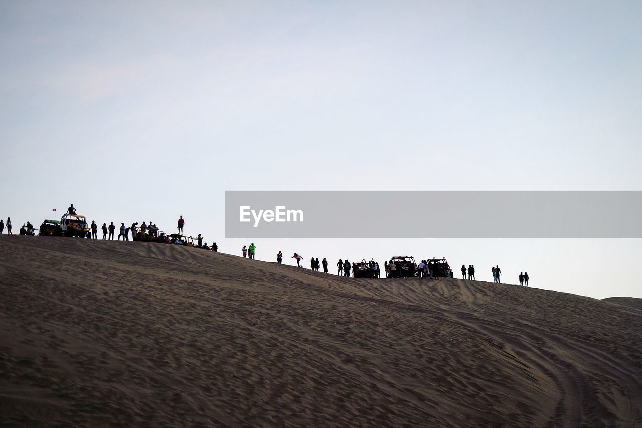 People on sand dune in desert against clear sky