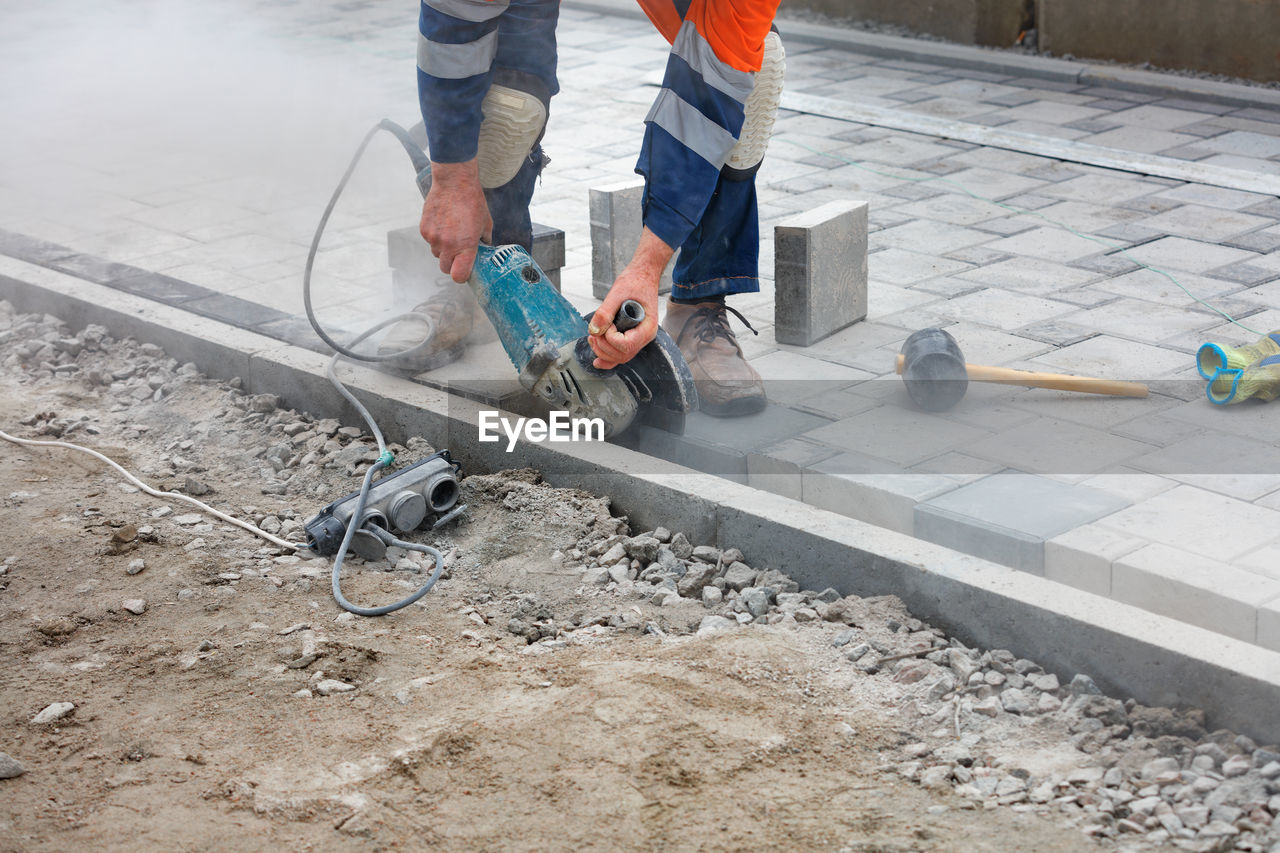 A worker with an electric grinder cuts paving slabs at a construction site.