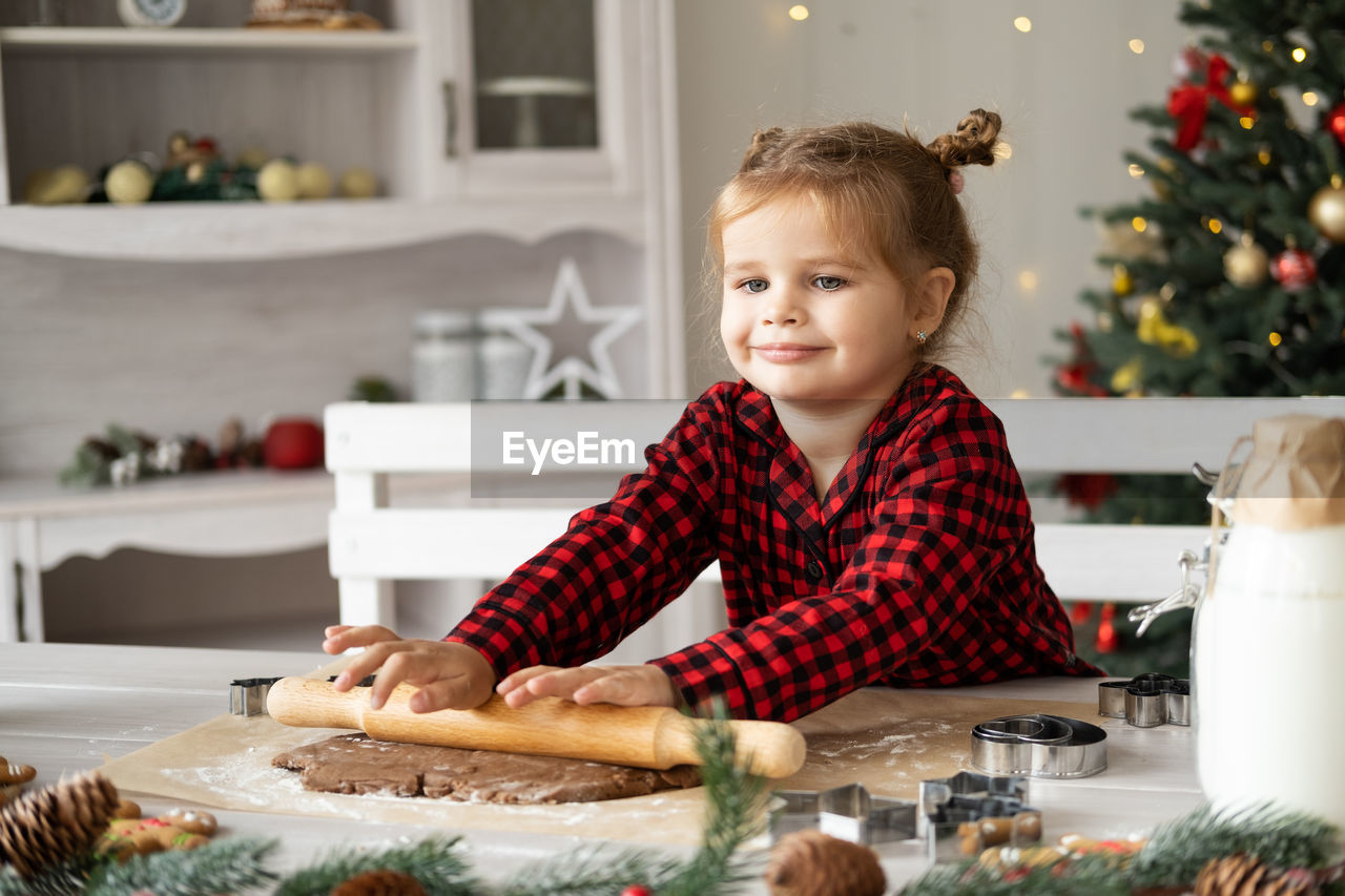 Little girl in red pajama cooking festive gingerbread in christmas decorated kitchen