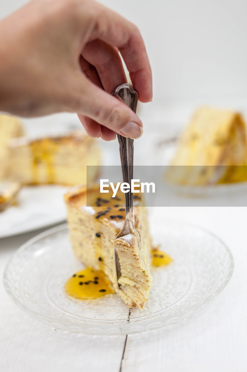 Cropped hand cutting dessert with fork on table