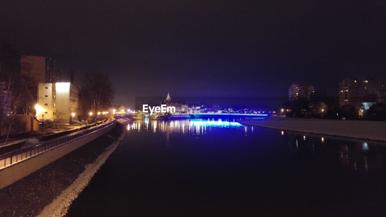 ILLUMINATED CITY BY RIVER AGAINST SKY