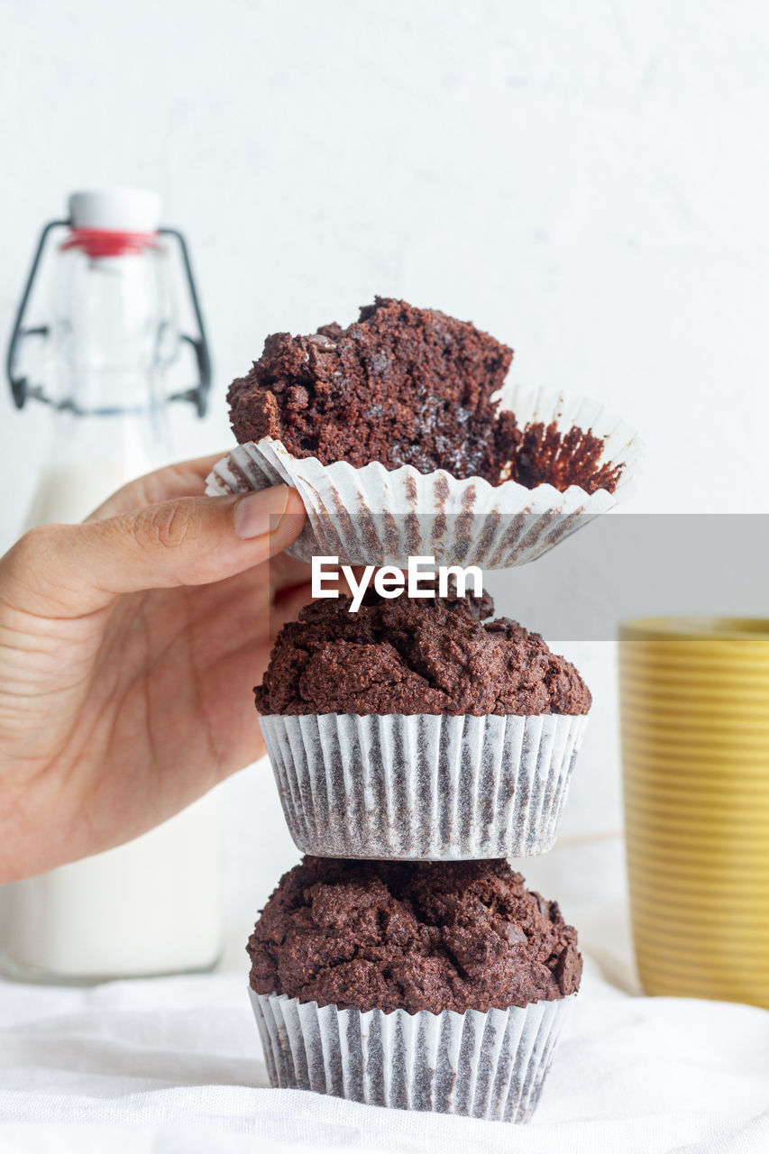 Crop anonymous person demonstrating delicious homemade chocolate muffins heaped on table in light kitchen person