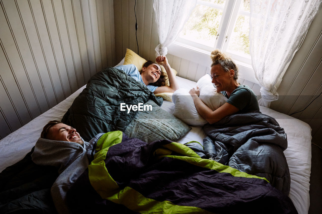 High angle view of cheerful male and female friends talking while lying on bed in cottage