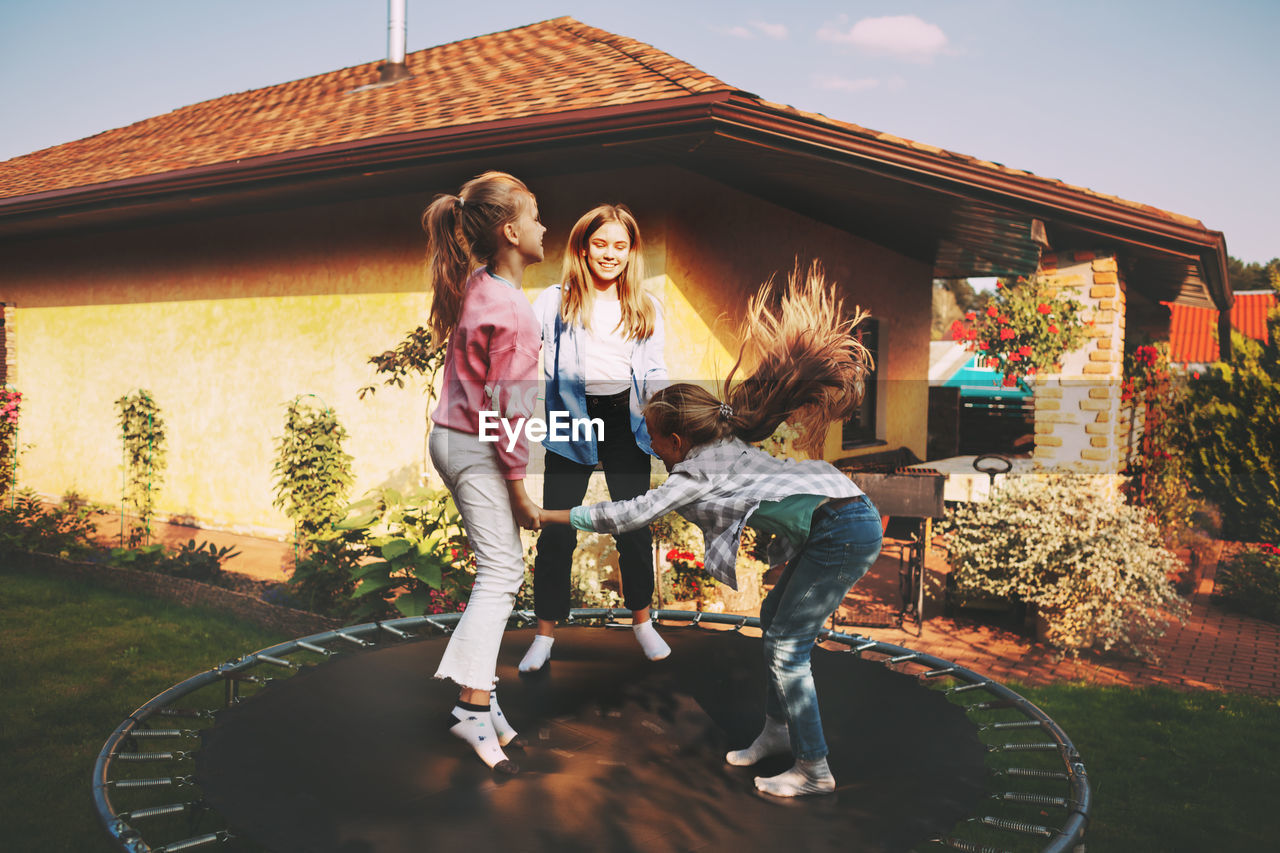 Happy three children are jumping on a trampoline in the garden near their house. 