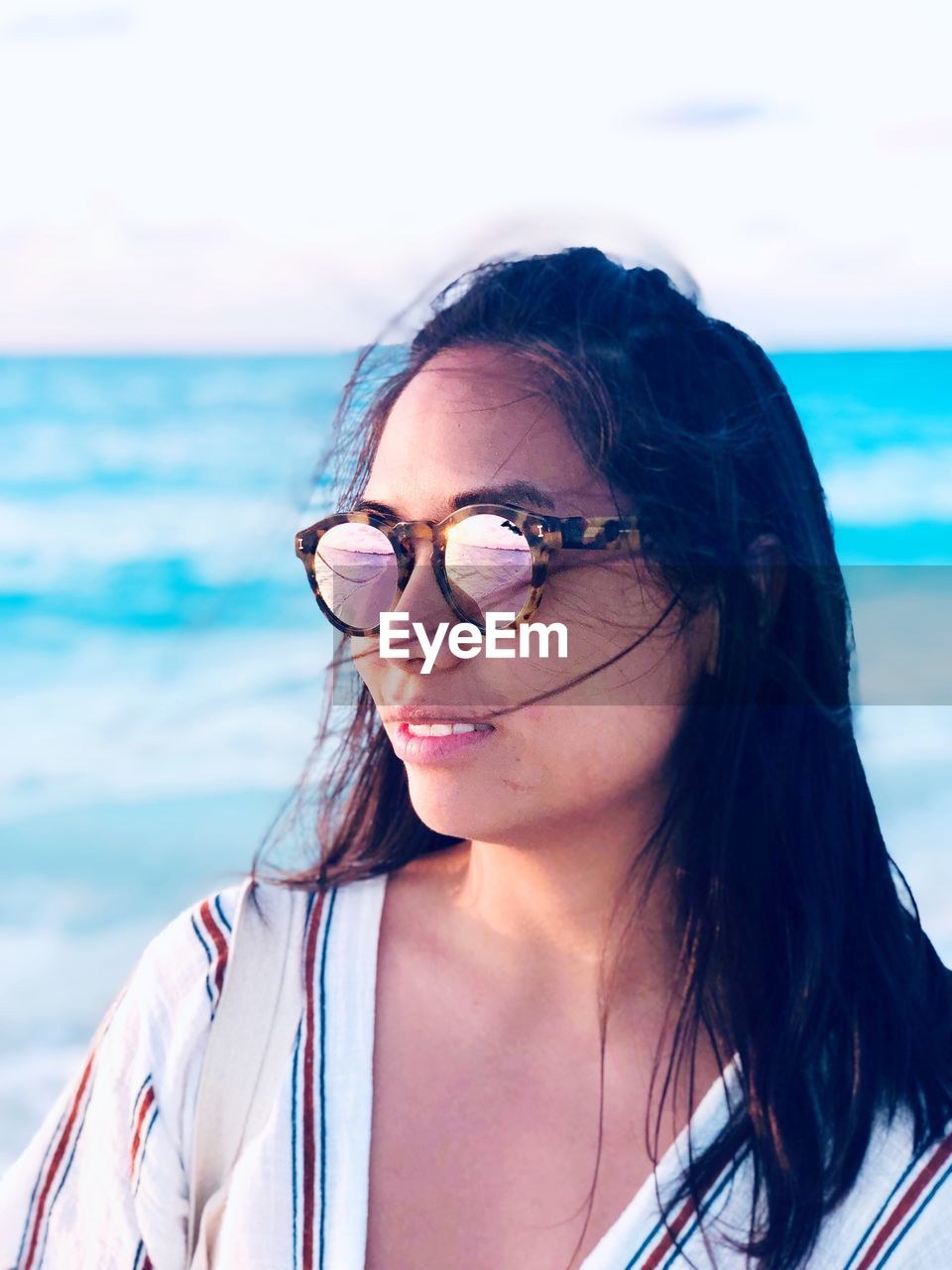 YOUNG WOMAN WEARING SUNGLASSES AGAINST SEA