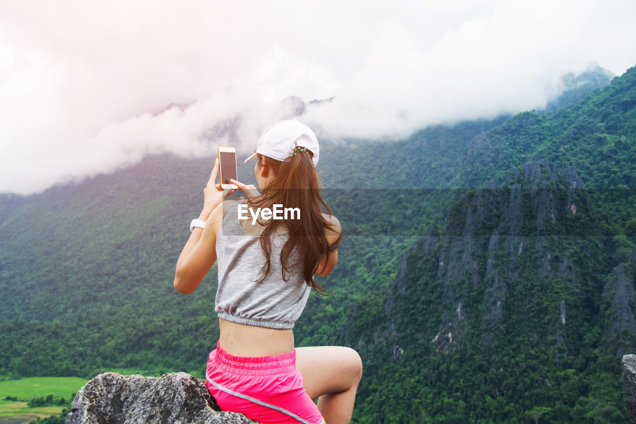 Rear view of woman standing on cliff against mountains