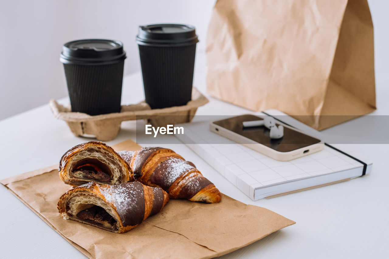 Chocolate croissants with cups of coffee and notepad with smartphone and earphones