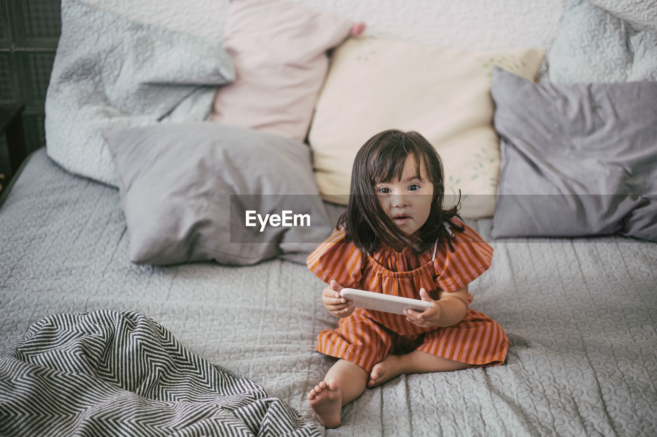 Portrait of down syndrome girl using digital tablet while sitting on sofa at home