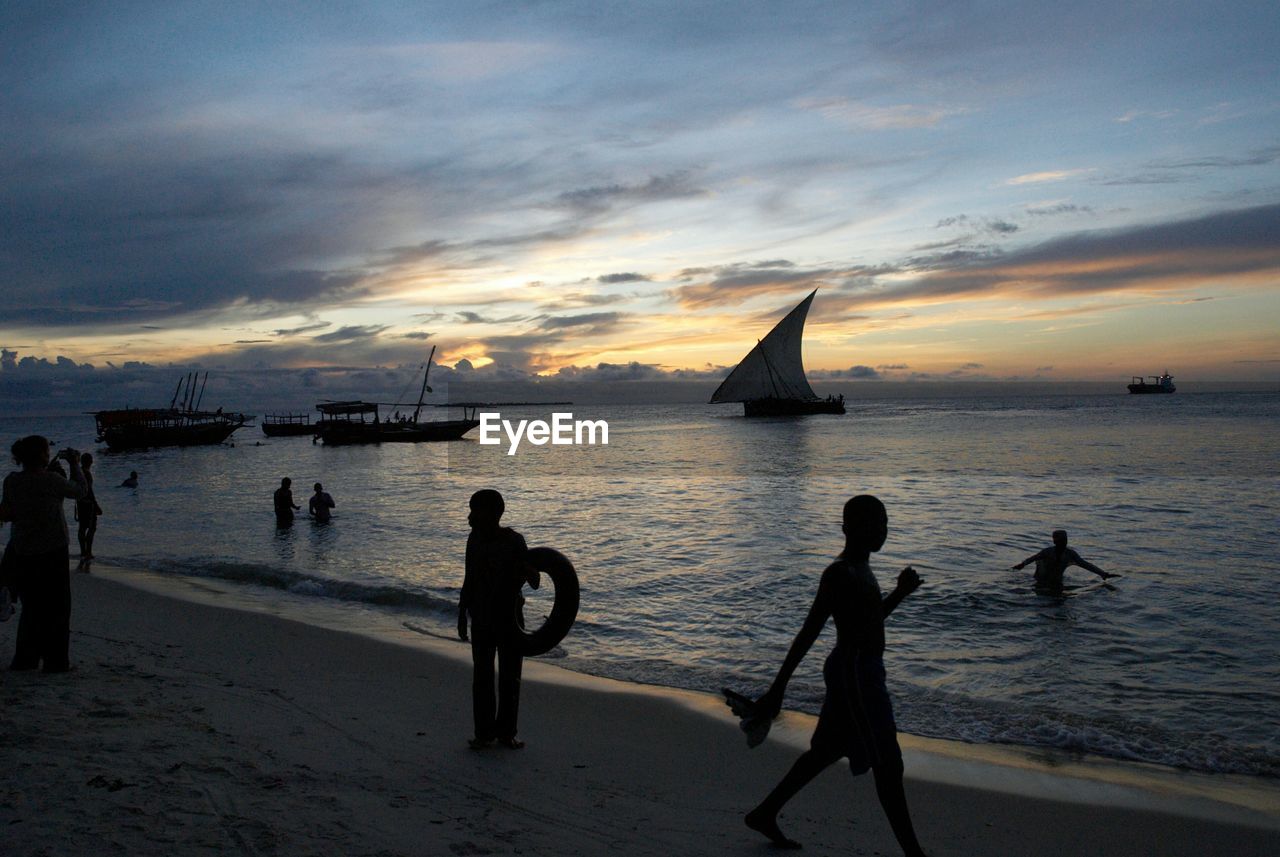 Silhouette people on beach against sky during sunset