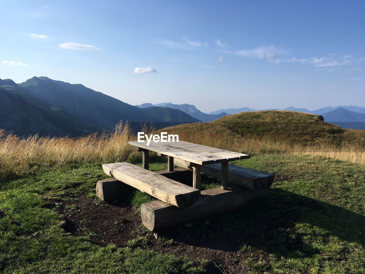 Bench on field by mountains against sky