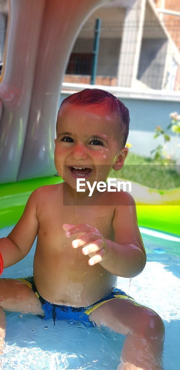 Portrait of smiling shirtless baby boy sitting in wading pool