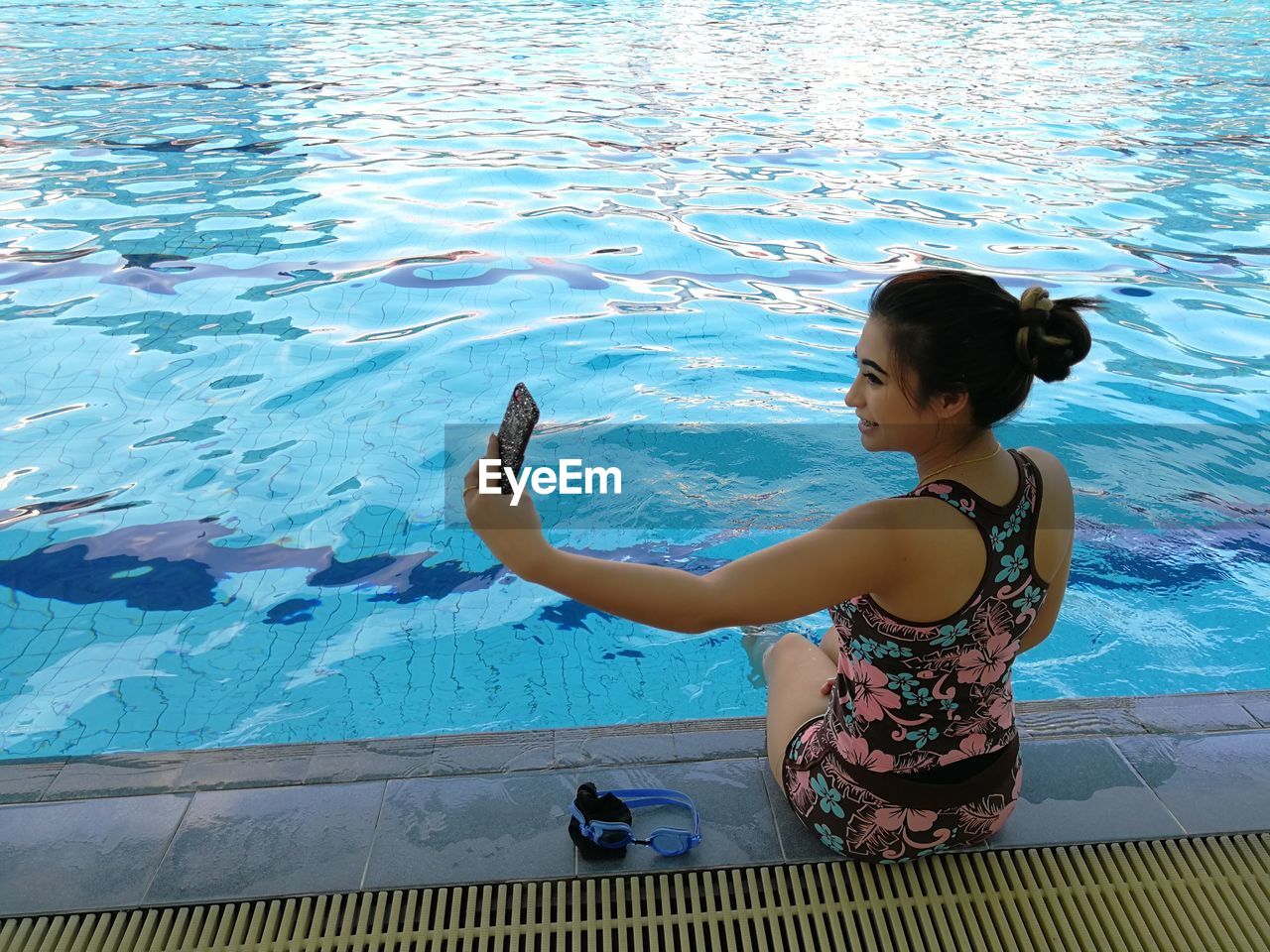 Young woman taking selfie while sitting at poolside