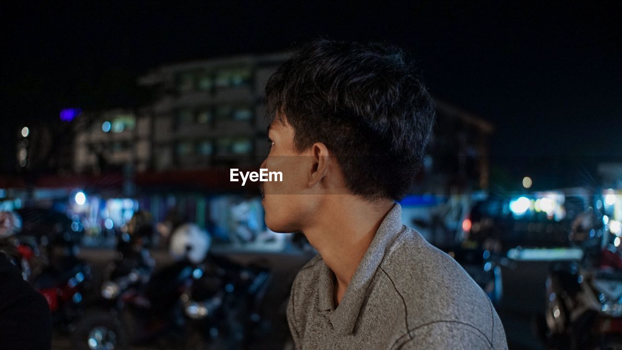 PORTRAIT OF MAN LOOKING AT CITY STREET AT NIGHT