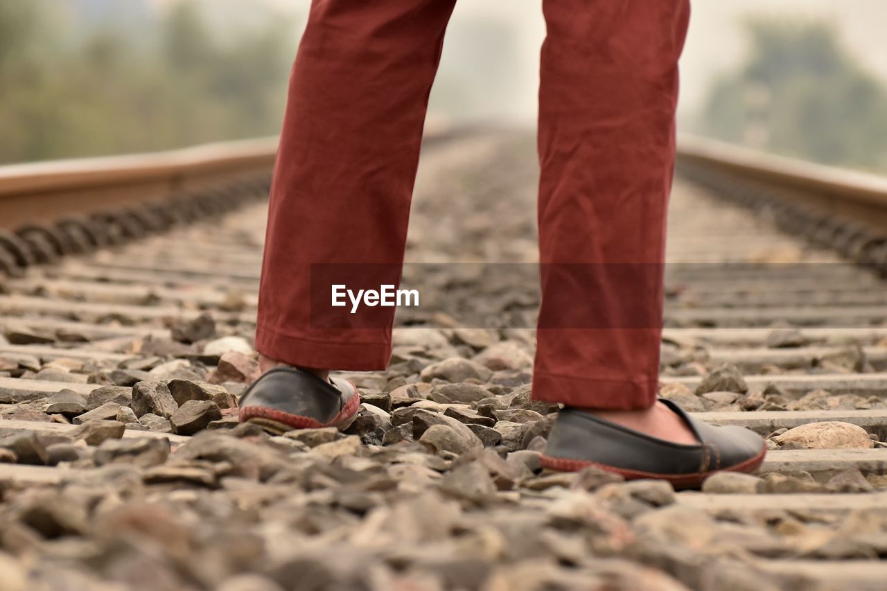 Low section of man standing on gravel at railroad track