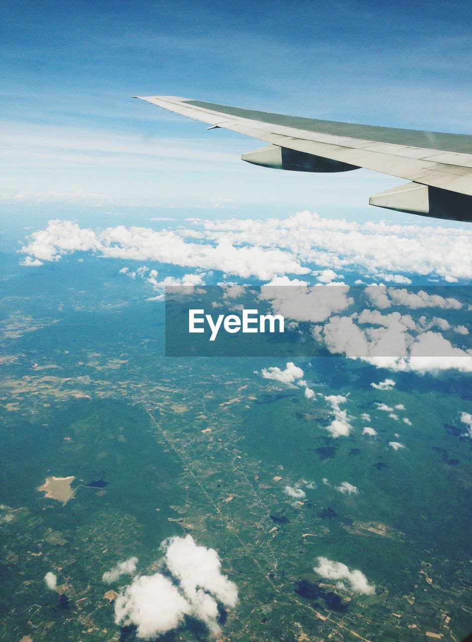 Aerial view of airplane wing over landscape against blue sky