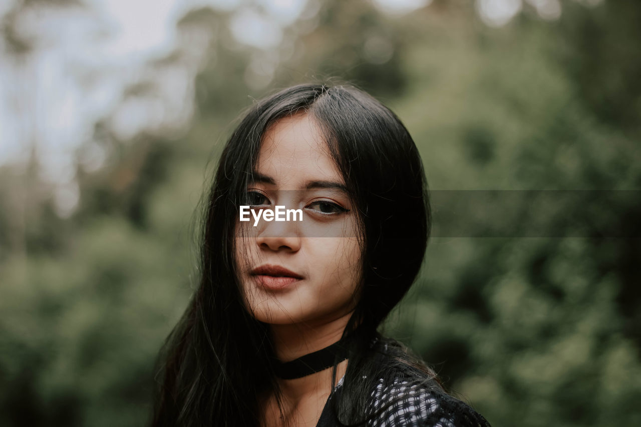 Portrait of young woman standing against trees