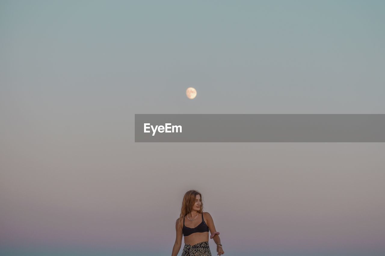 Rear view of woman standing against clear sky with full moon