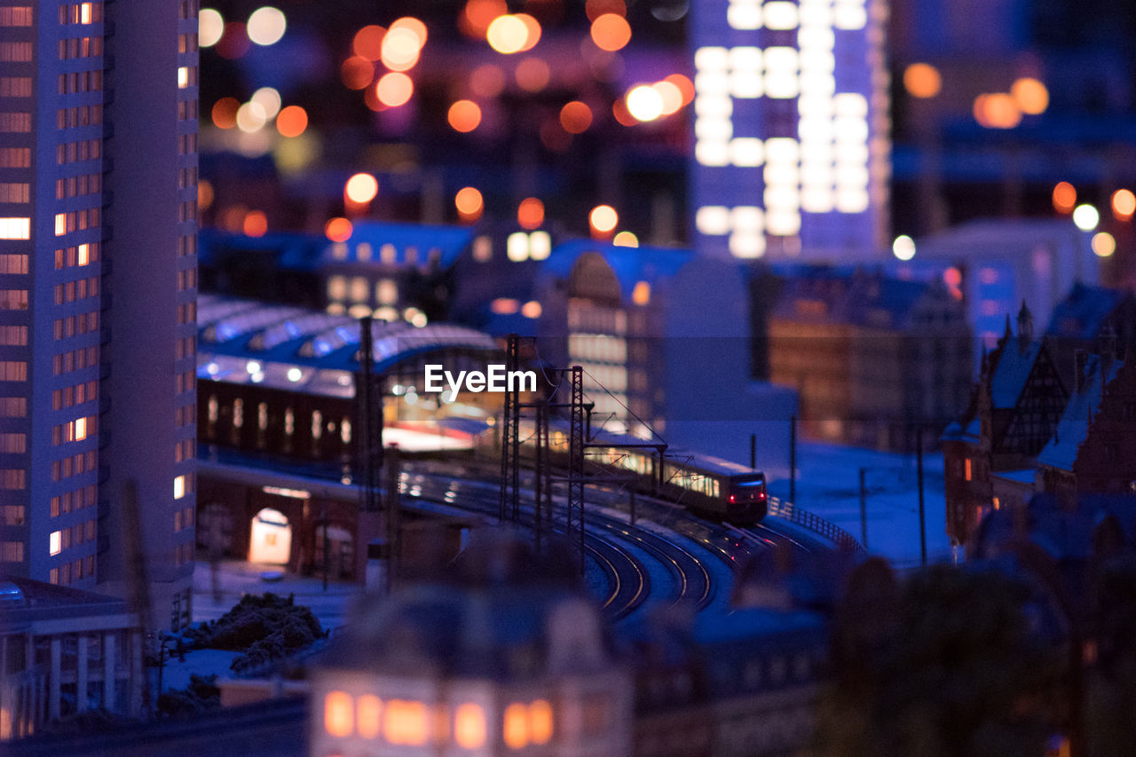 Tilt-shift image of train on railroad tracks in illuminated city