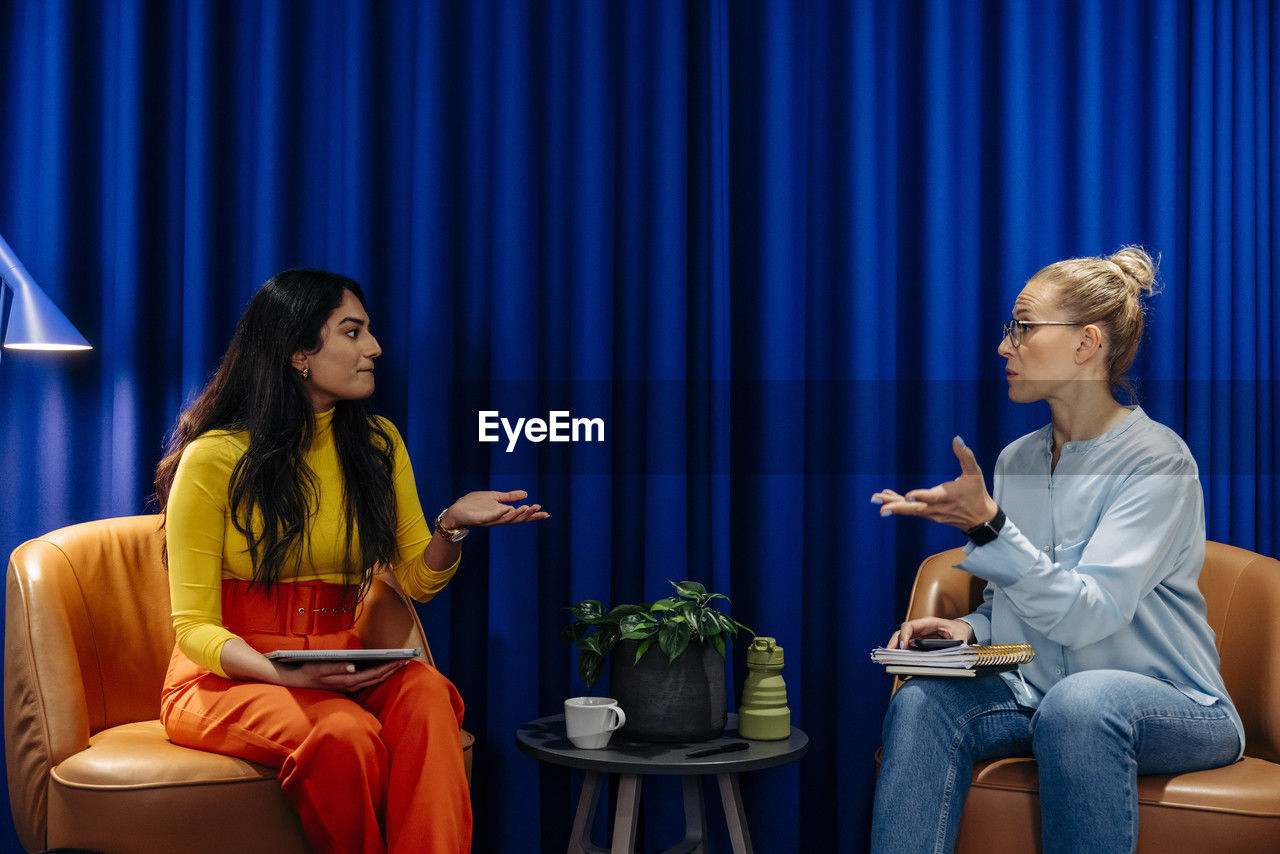 Businesswomen discussing with each other while sitting on chair at office