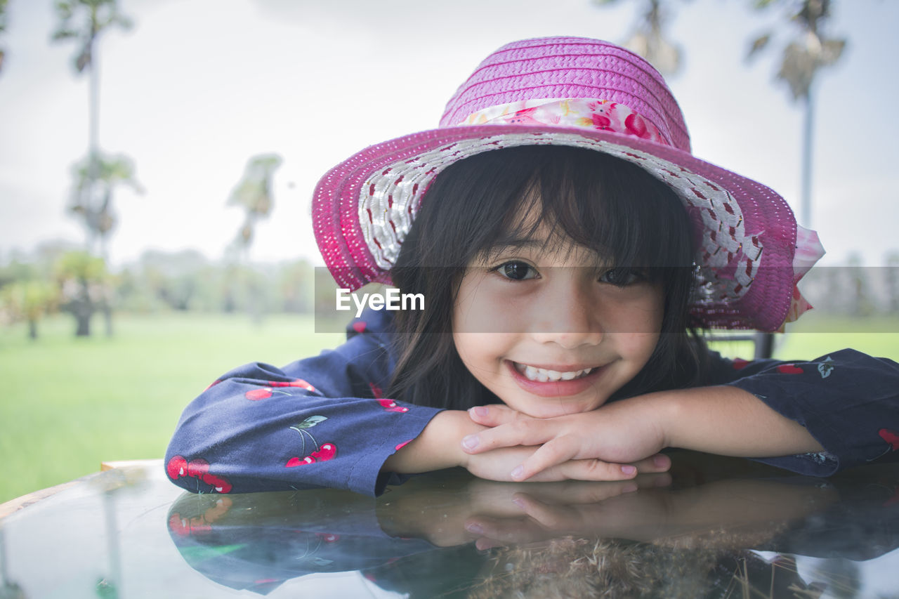Portrait of cute smiling girl wearing hat leaning on table against sky