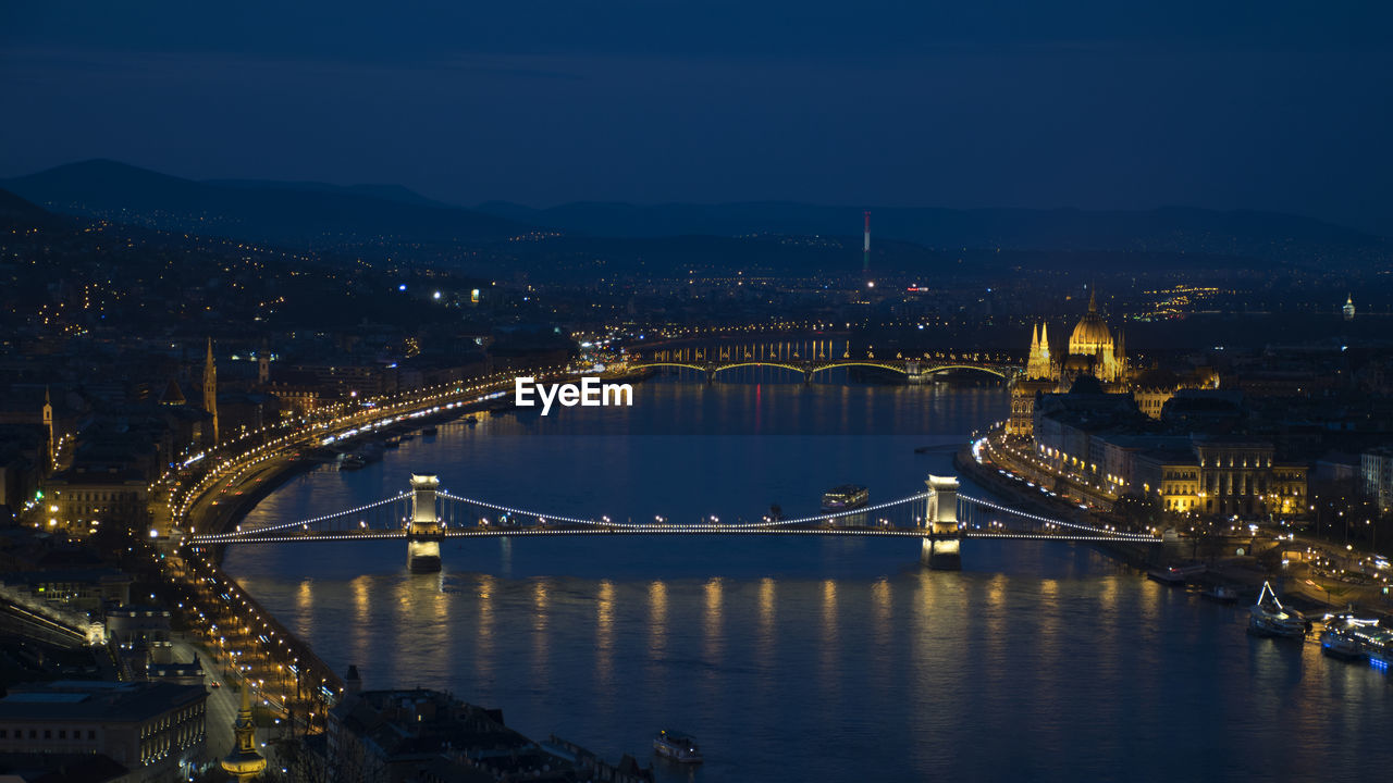 Illuminated bridge over river in city at night