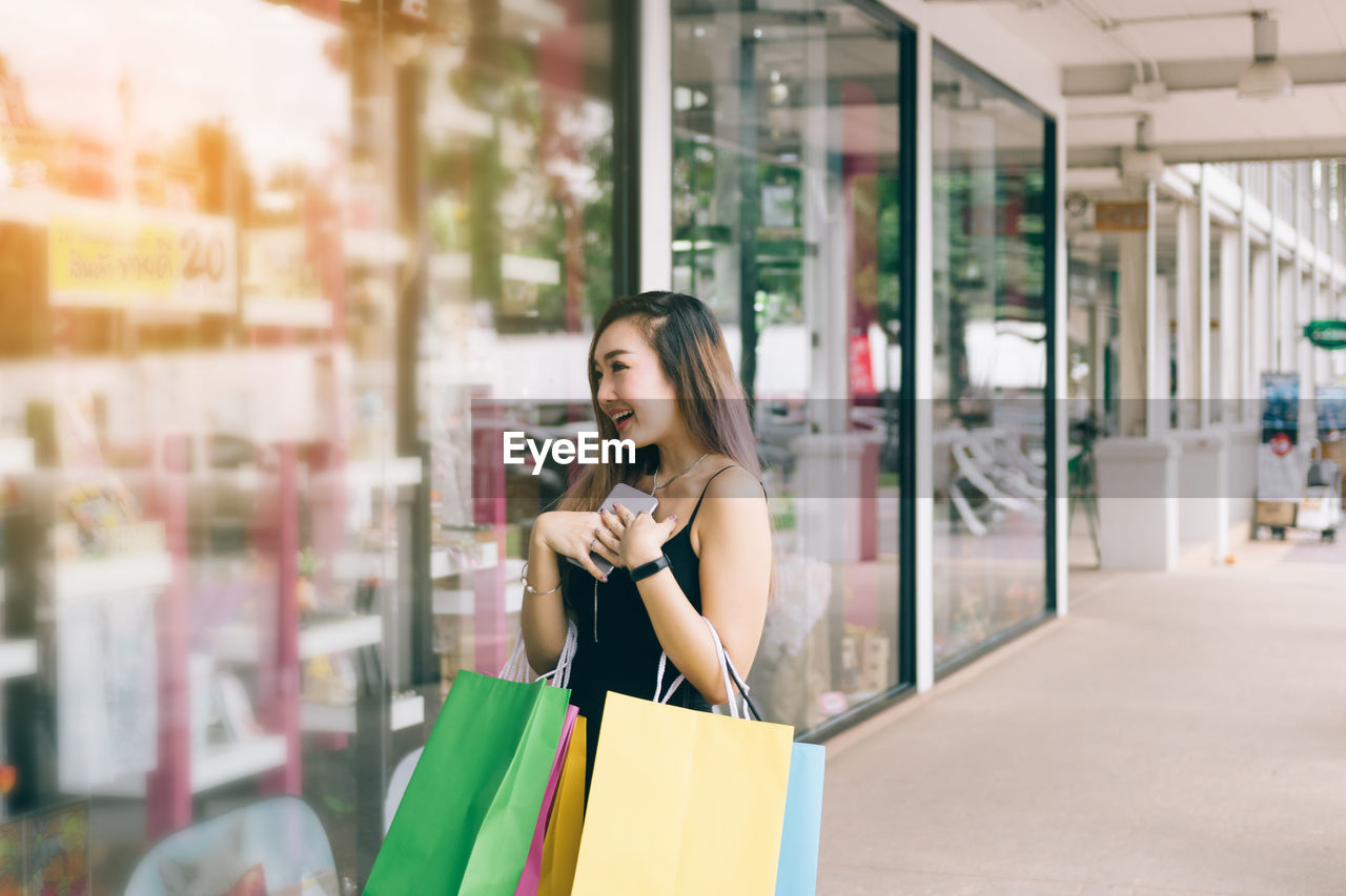 Young woman with shopping bags standing outside store