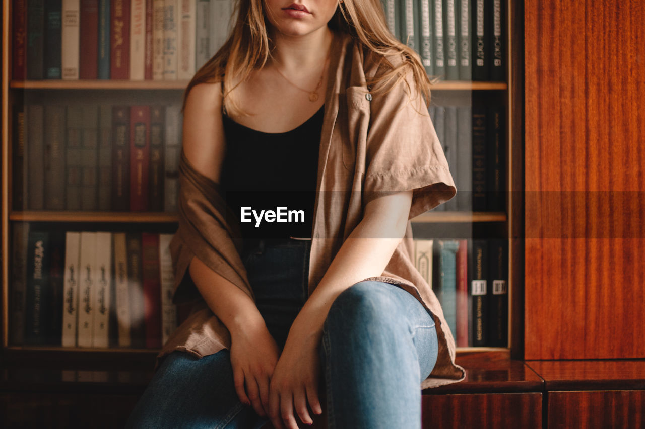 Cropped image of teenage girl sitting by bookshelf