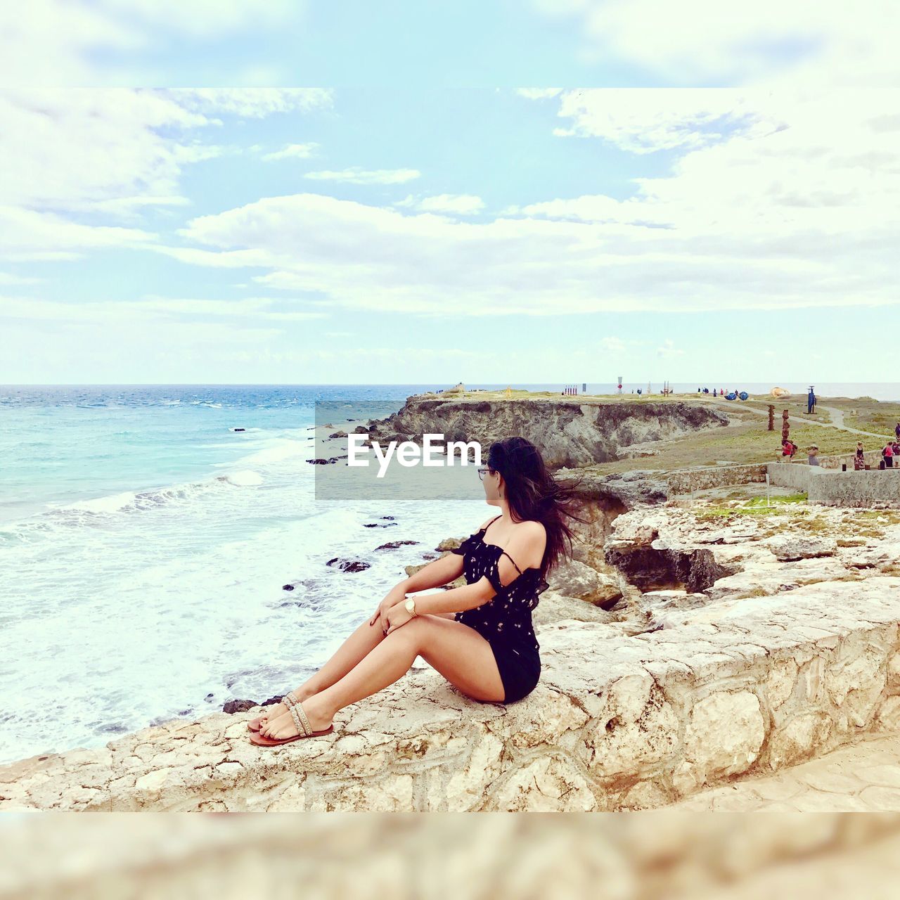 Side view of woman sitting on retaining wall at beach in isla mujeres