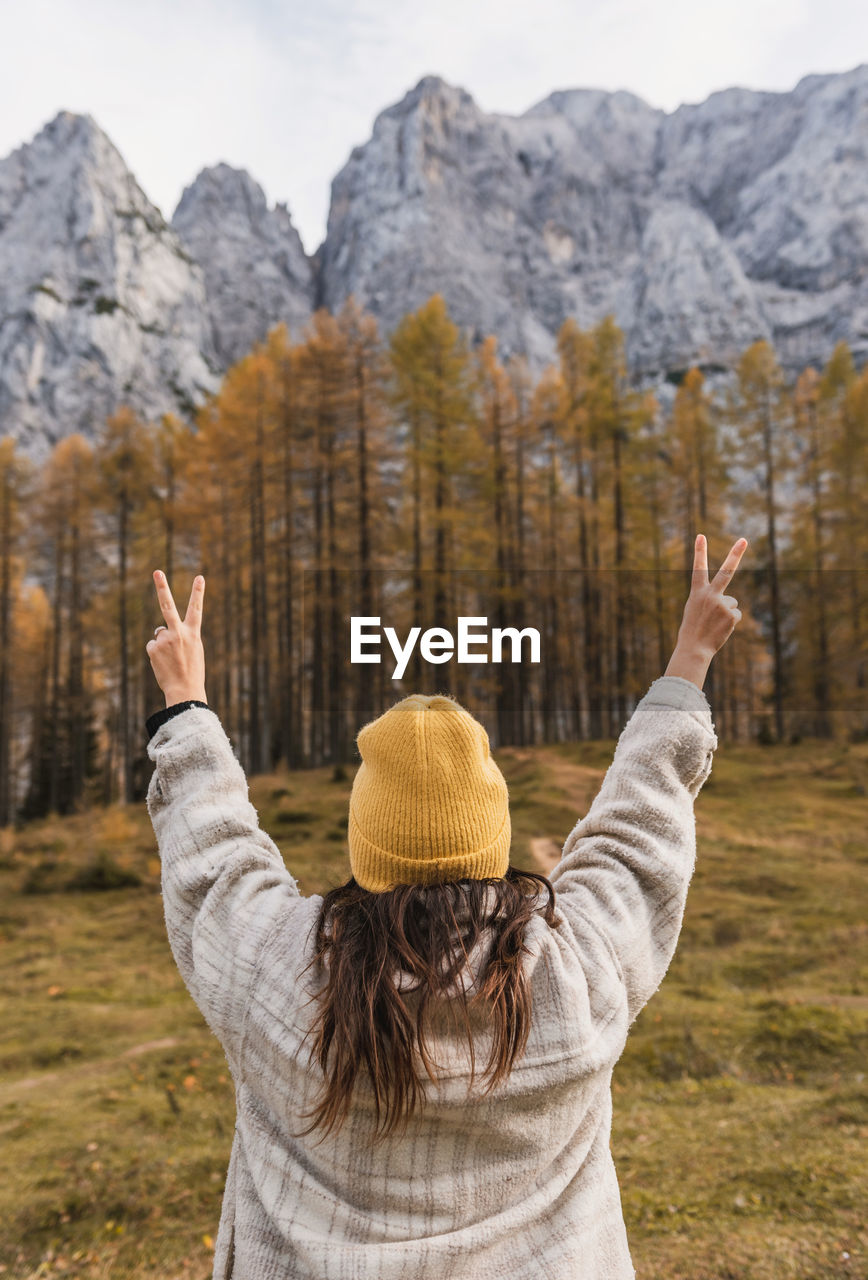 Rear view of young woman with raised arms standing under beautiful mountains in autumn