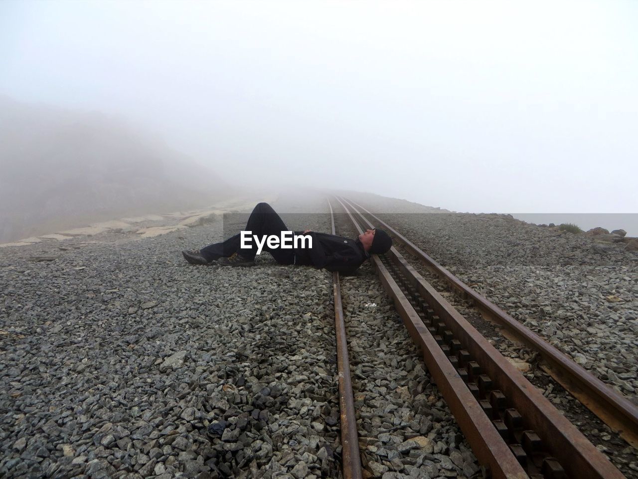 Full length of man resting on railroad track during foggy weather