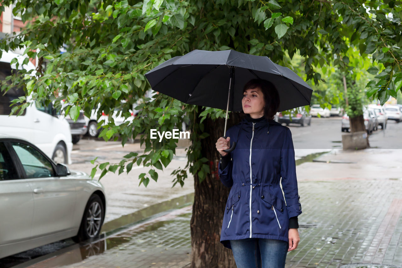 An adult woman with an umbrella walks down the street peering into people's faces  cloudy rainy day.